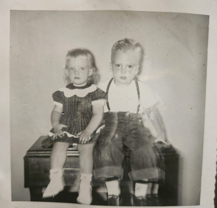 Young boy and girl sitting on sewing machine cabinet